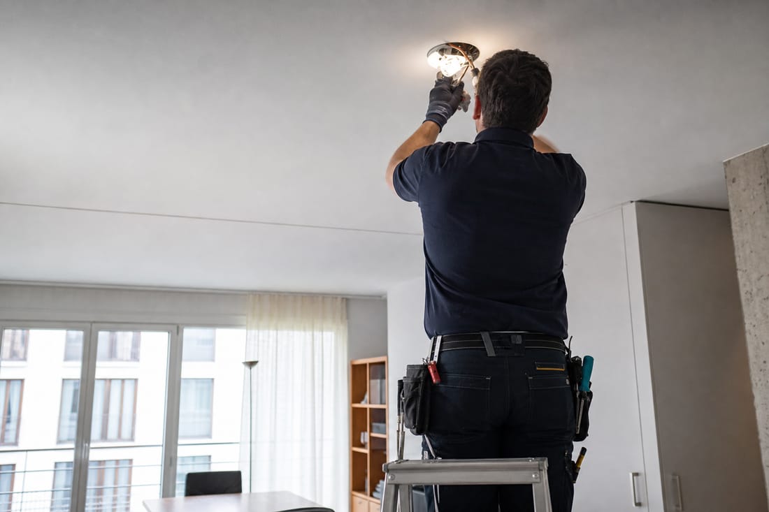Beispiel: Elektriker von hinten prüft eine Deckenleuchte